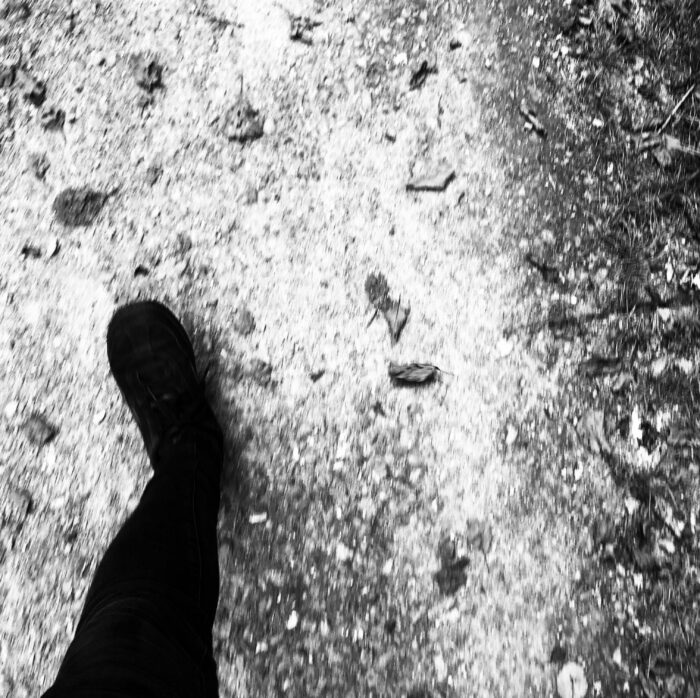 Ein Schwarzweiß-Bild eines linken Schuhs und des Beins, über Kiesel gehend